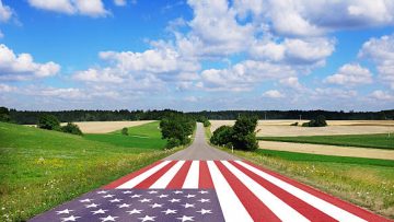 Country road with American flag, blue sky with white clouds.