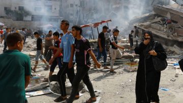 Palestinians walks near the rubbles in the aftermath of Israeli strikes