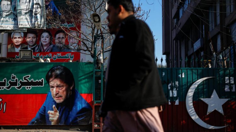 People walk past a banner with a picture of the former Prime Minister Imran Khan outside the party office of Pakistan Tehreek-e-Insaf (PTI), a day after the general election, in Lahore